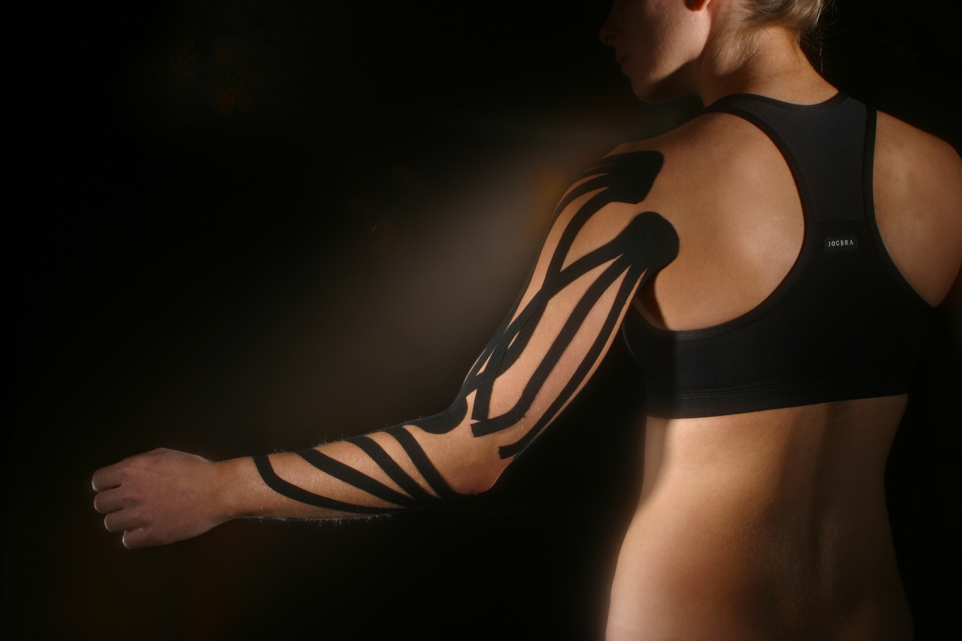 A woman in a jog bra with therapeutic kinesio tape on her arm